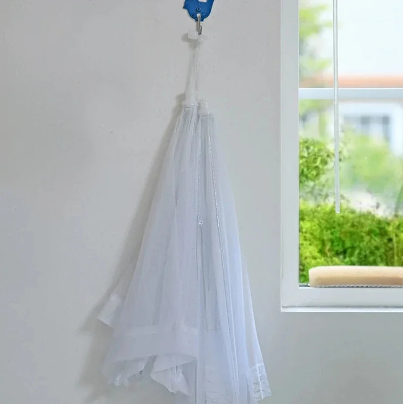 The OWOW Me Best foldable anti-fly screen mesh for food in white is displayed hanging from a blue hook on a white wall by a window with greenery outside.