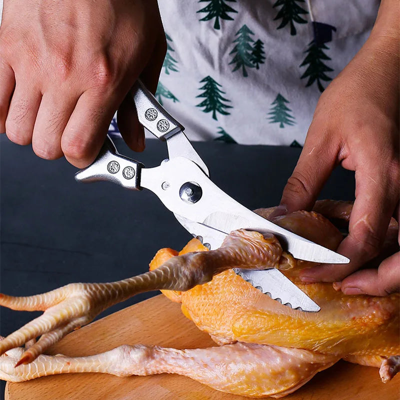 Wearing an apron with a green tree pattern, a person uses OWOW Me Stainless Steel Poultry Bone Cutter Scissors to cut raw poultry on a wooden cutting board.